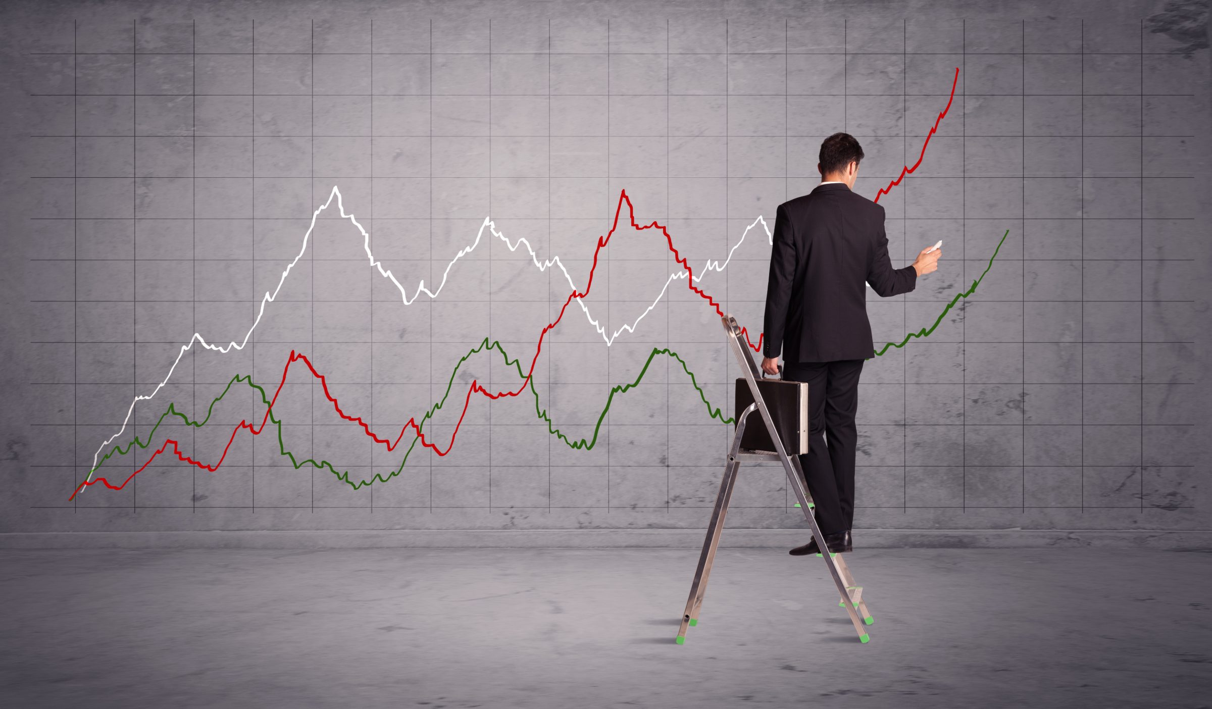 A businessman on a stepladder drawing rising line charts on a grey concrete grid wall