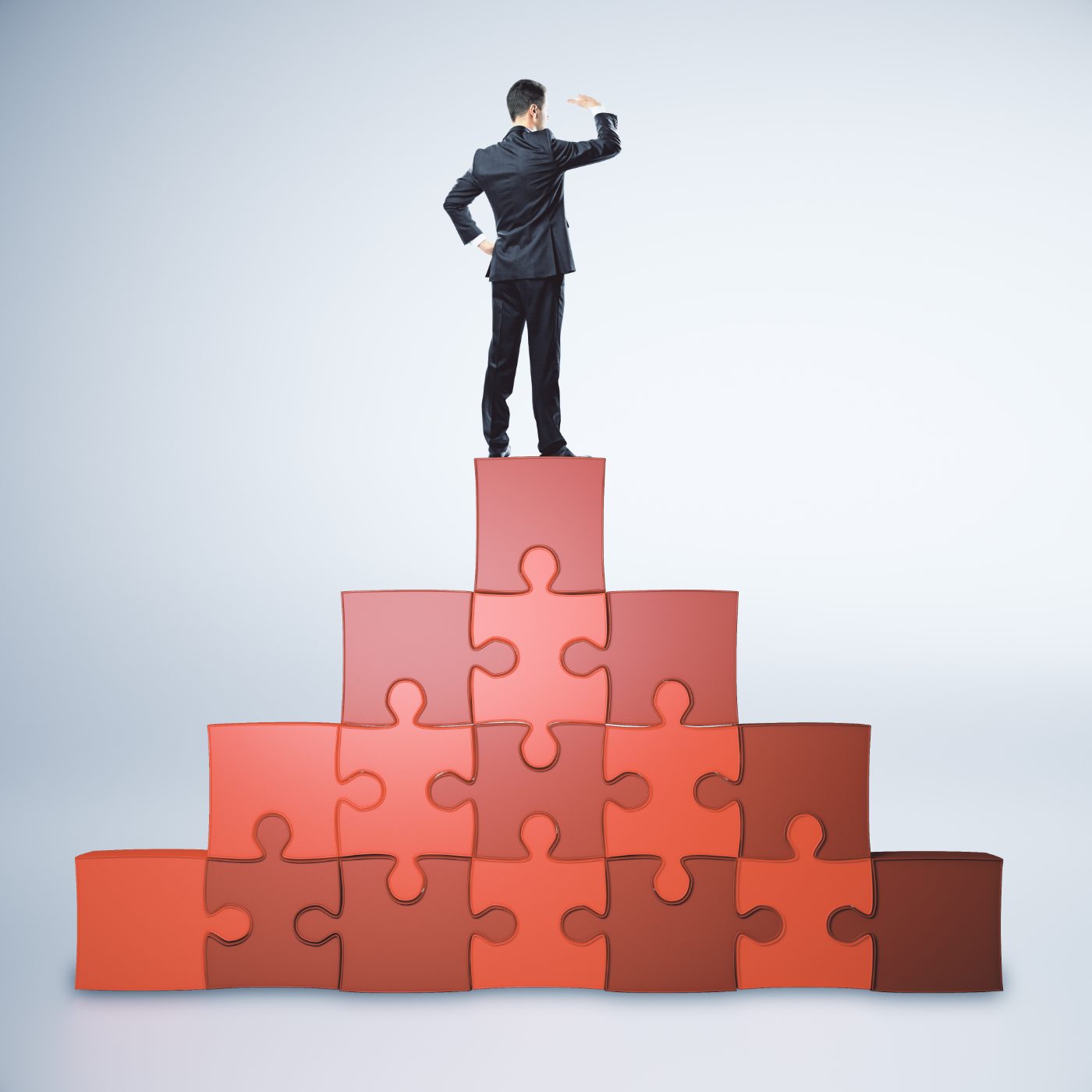 A businessman standing on top of a red jigsaw-puzzle pyramid, shading his eyes and looking into the distance